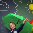 Primary Pupil Holding An Umbrella Standing In Front Of Different Seasons and Types Of Weather