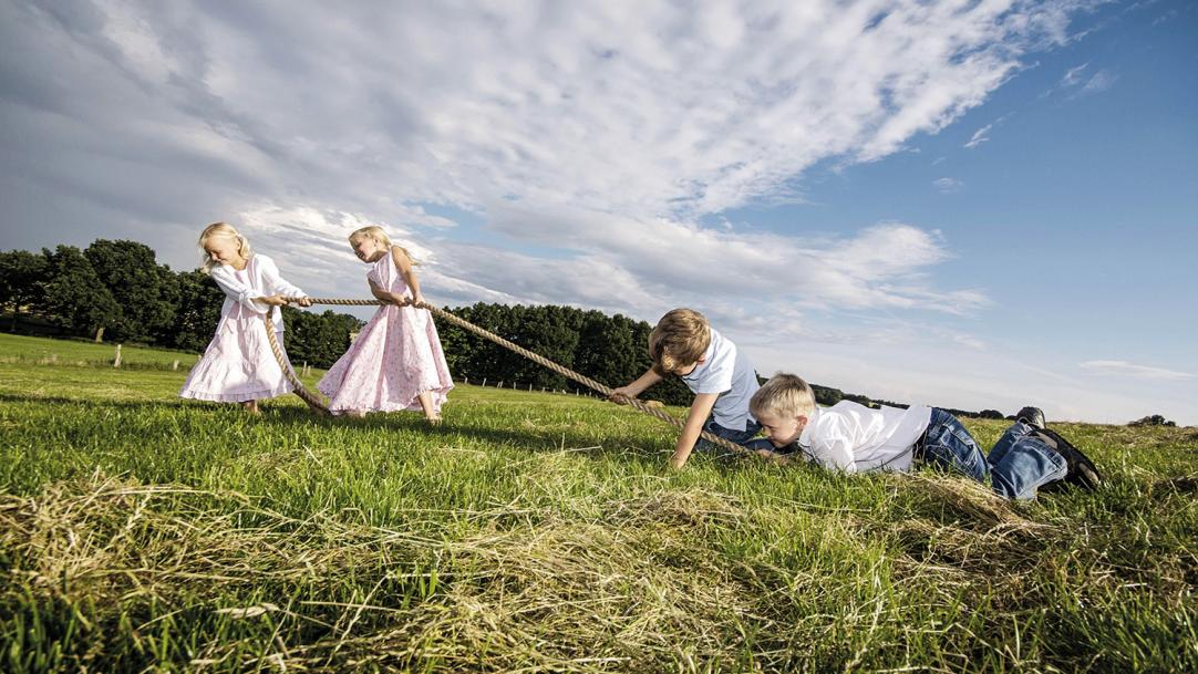Two girls beating two boys at tug of war on a grassy hill - gender gap reading