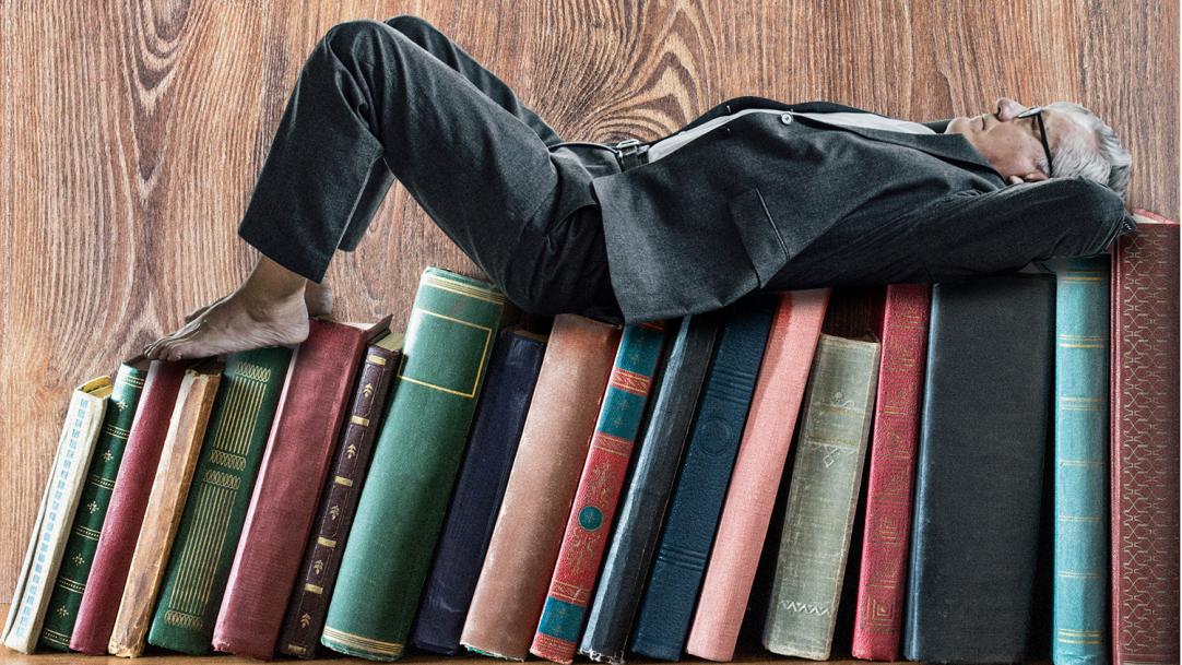 A man lying on a shelf of books – reading relaxation teachers