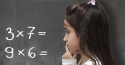 Primary Aged Pupil Looking At Maths Multiplication & Division Question On The Board