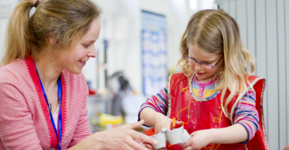 Teacher supporting young pupil practicing scissor skills