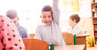 Boy Raising Hand To Answer A Question To A Fun End-Of-Term Activity In Primary Classroom