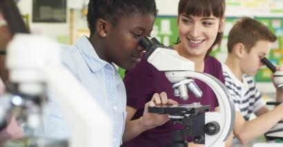 Student looking down a microscope, teacher supporting students in science