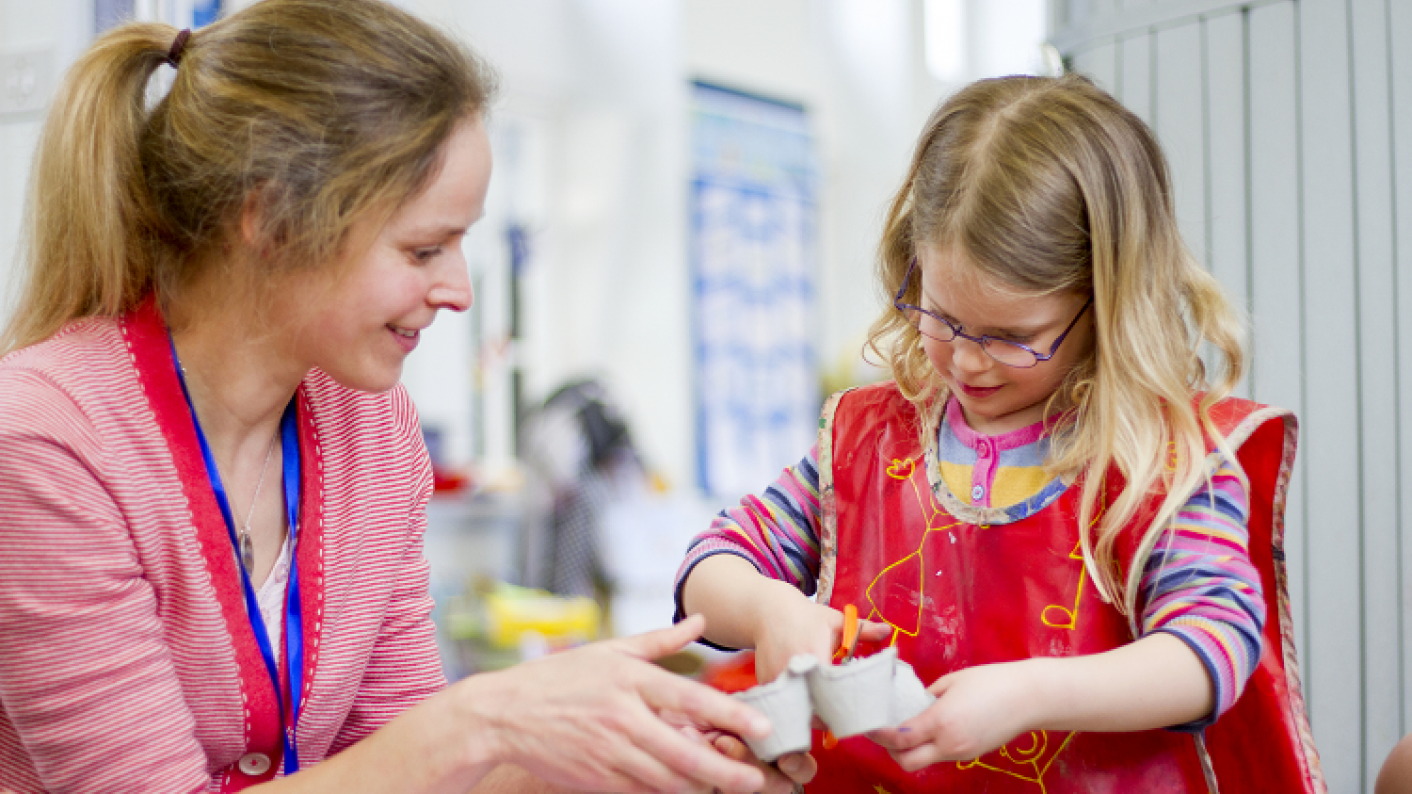 Teacher supporting young pupil practicing scissor skills