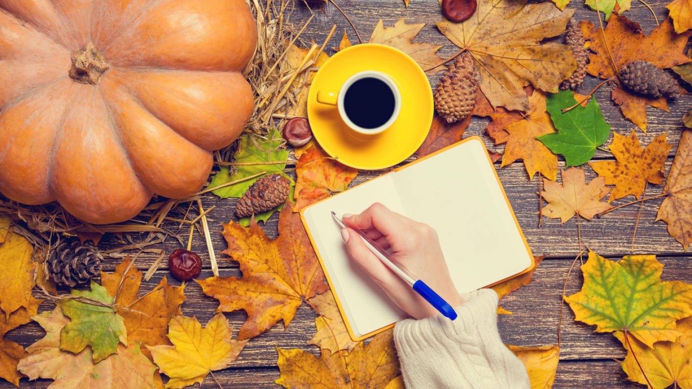 Autumn leaves on a table and a person writing autumn poetry