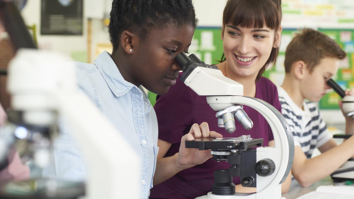 Student looking down a microscope, teacher supporting students in science