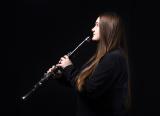 Teenage girl plays the clarinet, against dark background