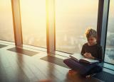 Boy reads book in front of large window in luxury flat