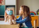 Young girl at nursery school plays with a cuddly rabbit that's wearing a face mask