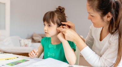 child sitting with adult as they adjust their hearing aid