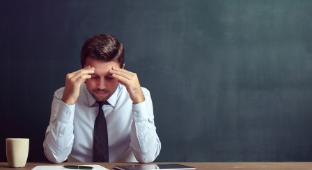 Teacher hunched at desk with head in hands