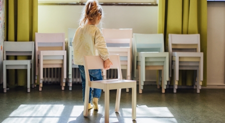 Child pulling chair away with back to camera