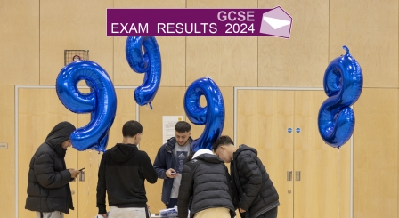 Several teenage boys looking at a table with balloons of 9s and 8s in the background