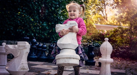 Small girl playing with life sized chess pieces