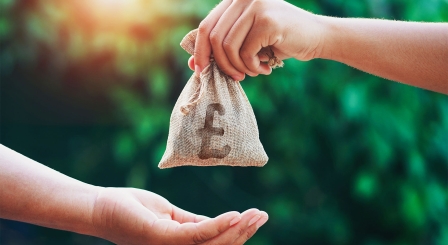 Someone handing a bag with a British pound sign on it to another person