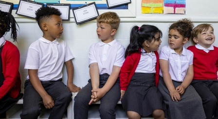 Primary school children sit along a bench