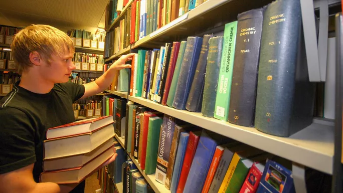 A-level exam dates 2024 – A-level student in library with stack of books