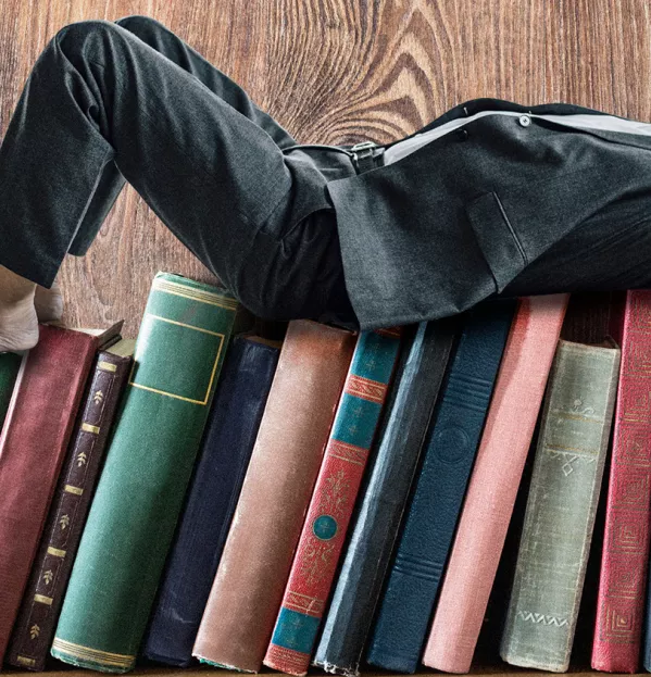 A Man Lying On A Shelf Of Books – Reading Relaxation Teachers