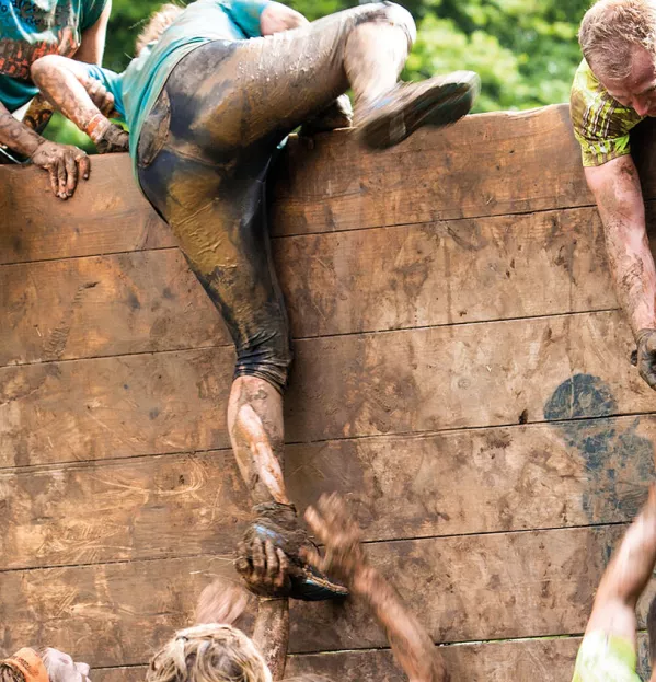 A Team Helping One Another Over A Wall In A Muddy Obstacle Course - Teamwork Crisis
