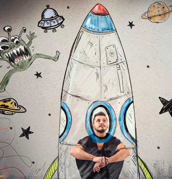 Man In A Drawing Of A Rocket Surrounded By Stars, Planets & Aliens – Deprived Students College Partnerships Scholarships