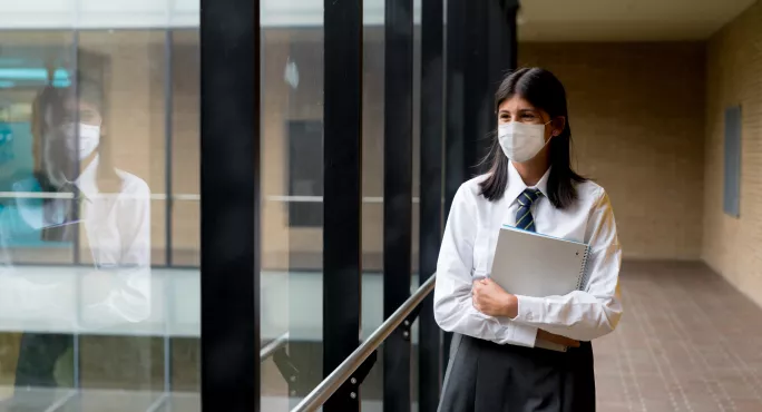 pupil with mask holding books and looking out of window