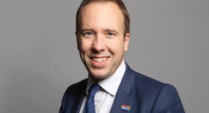 Matt Hancock in a suit smiling against a grey background 