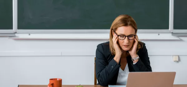 teacher sat in front of chalk board with head in hands and eyes closed
