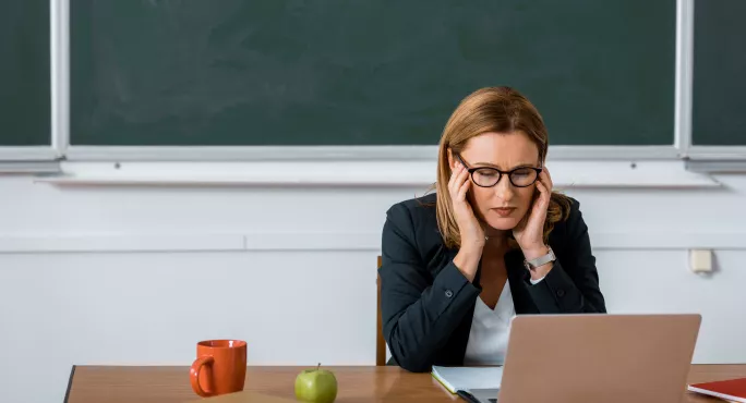 teacher sat in front of chalk board with head in hands and eyes closed