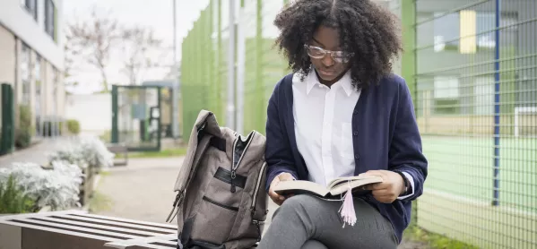 secondary pupil sits on bench reading 