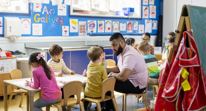 reception class sit at table with teacher 