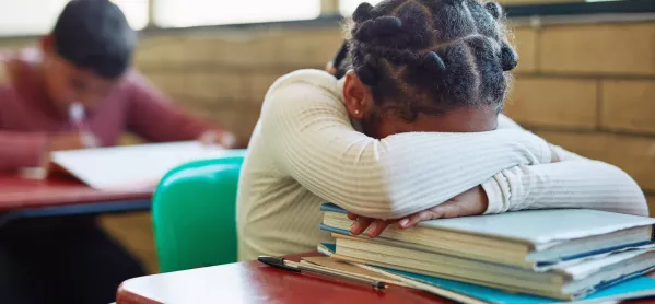 Child sits with head in arms on top of textbooks pile 
