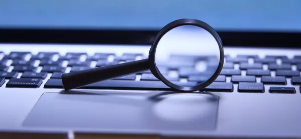 a magnifying glass rests on a laptop keyboard 