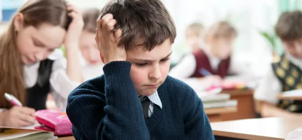 young pupil sits at test holding hair in frustration 