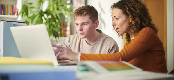 teacher assists pupil on laptop 