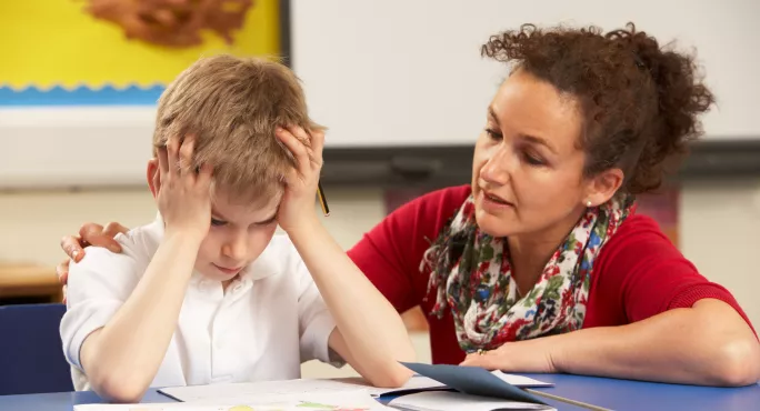 Frustrated school boy working with teacher in the classroom