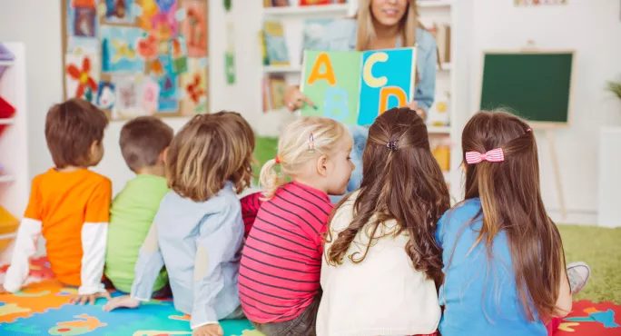 Nursery pupils sat on mat in front of teacher with alphabet letters