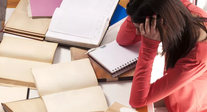 Teacher sits with head in hands in front of books