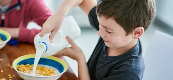 Young pupil pours milk into cereal bowl