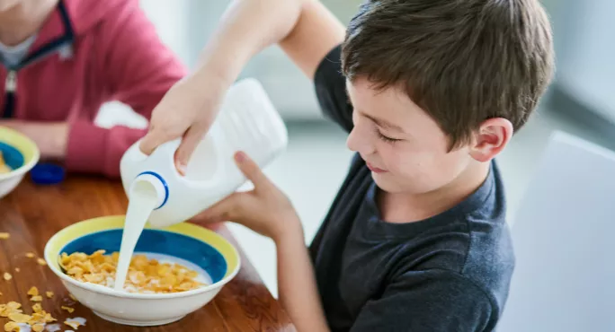 Young pupil pours milk into cereal bowl