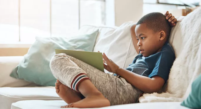 Child reading book on a sofa in blue top