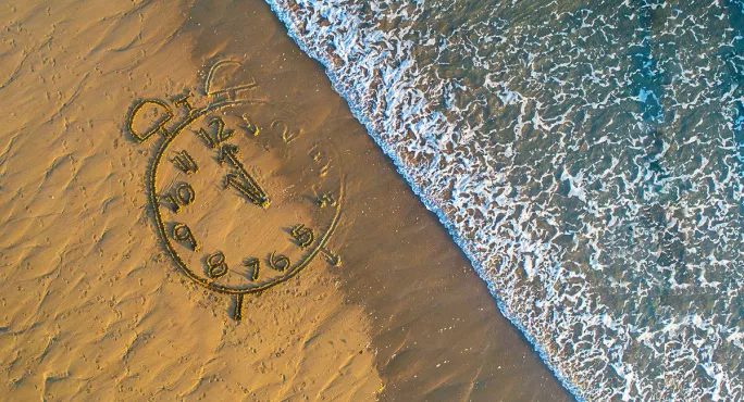 Clock drawn in sand with sea coming in from above 