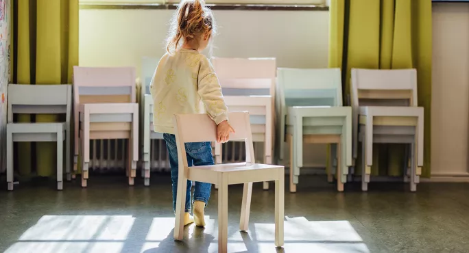 Child pulling chair away with back to camera