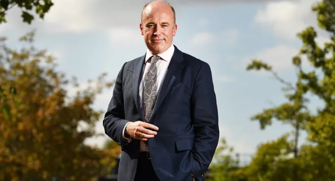 Jon Coles stands in nature setting with suit and tie