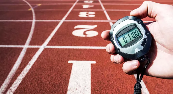 person holding timer showing 11 minutes against backdrop of athletics track