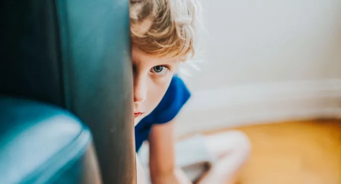 child peeping out from behind chair