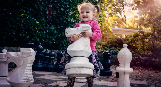 Small girl playing with life sized chess pieces