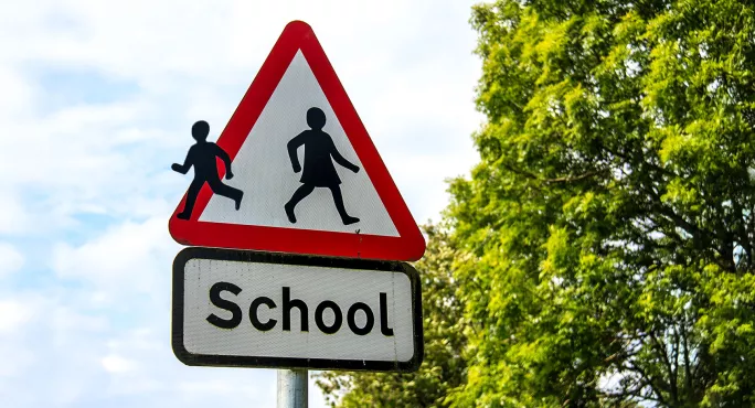 A school road sign with one of the figures running away