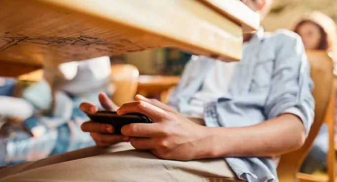Student looking at mobile phone under desk