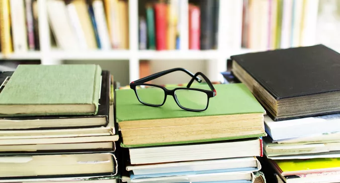 A pair of glasses on top of three piles of books