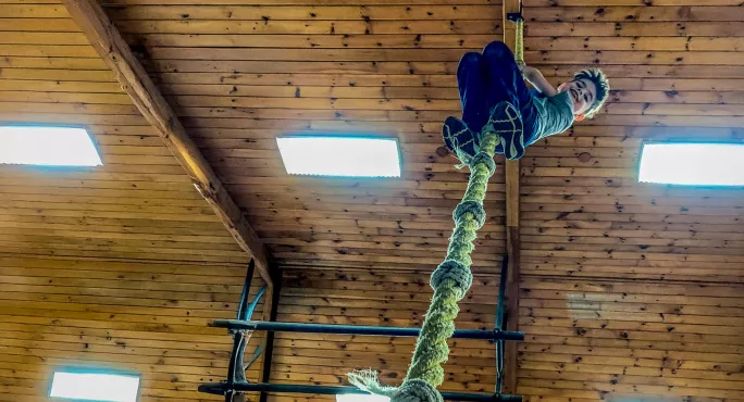 School child climbing gym rope